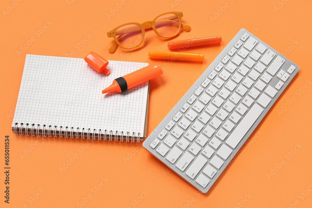 Blank open notebook with eyeglasses, markers and keyboard on orange background