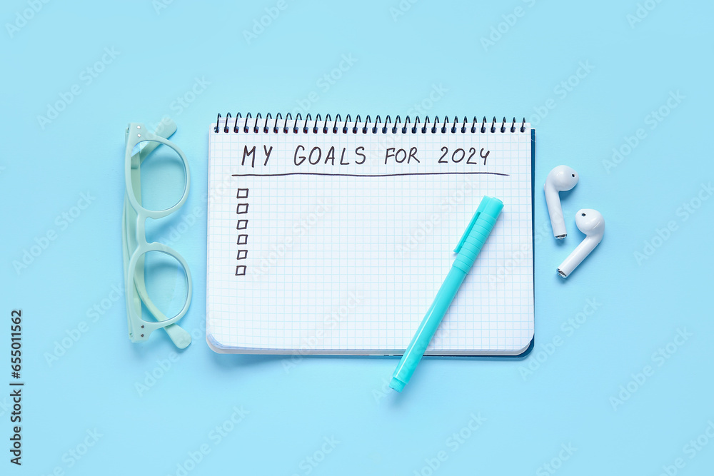 Notebook with empty to do list, eyeglasses and earphones on blue background. New year goals