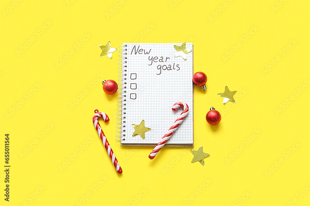 Notebook with empty to do list, candy canes and Christmas balls on yellow background. New year goals