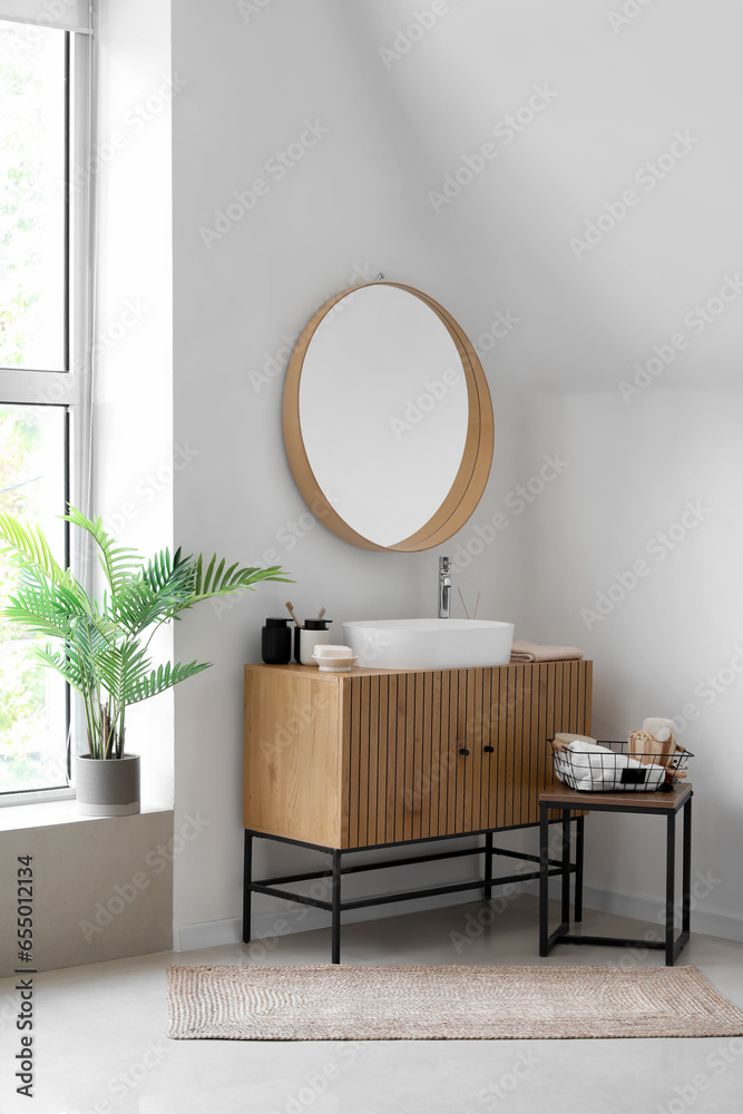 Sink bowl and bath accessories on wooden cabinet in interior of light bathroom