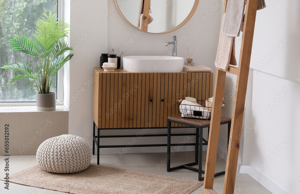 Sink bowl and bath accessories on wooden cabinet in interior of light bathroom