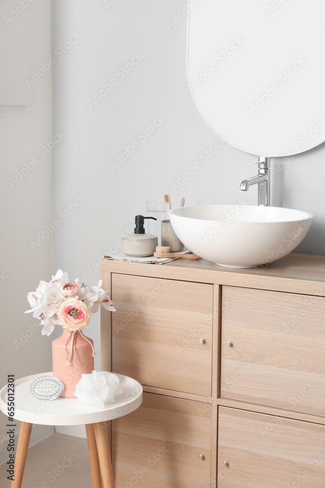 Interior of light bathroom with sink bowl, bath accessories and ranunculus flowers