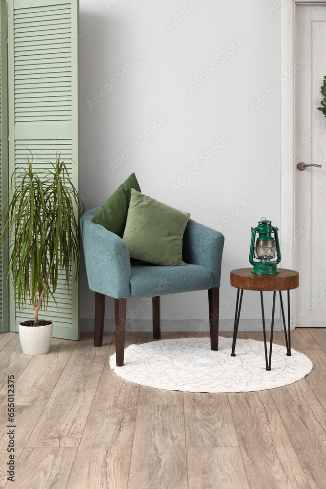 Interior of living room with blue armchair, folding screen, houseplant and stool