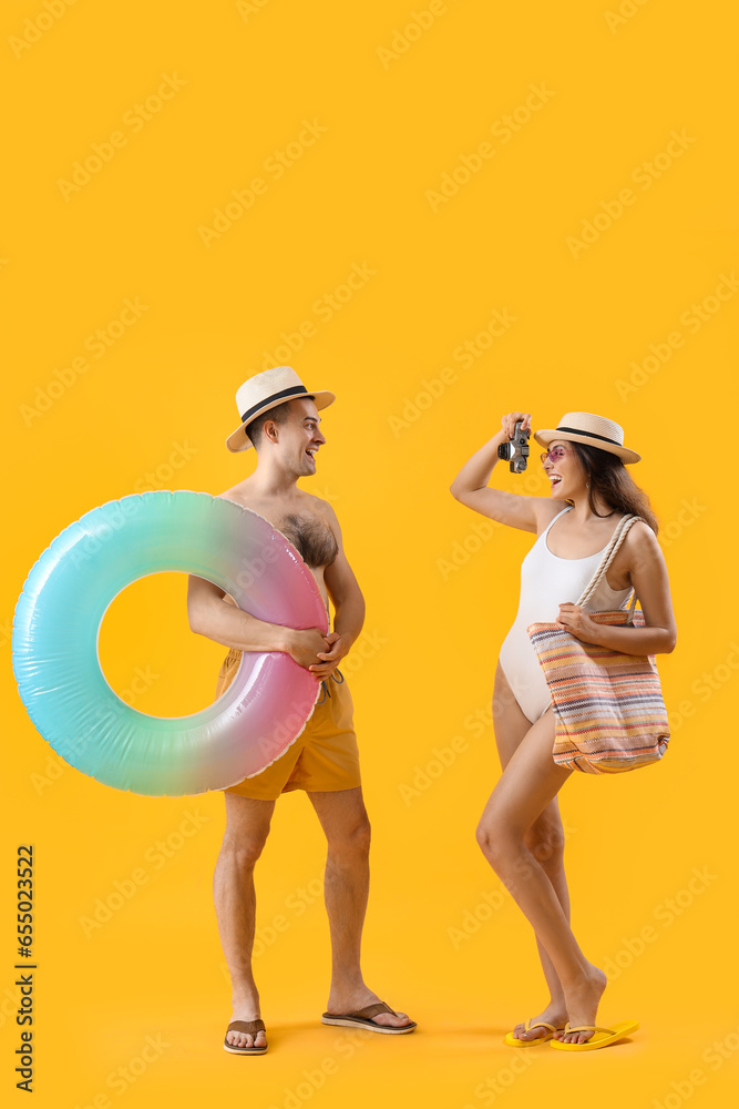 Young couple with inflatable ring and photo camera on yellow background