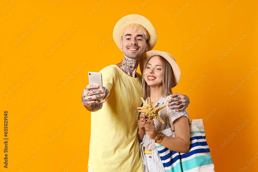 Young couple with starfishes taking selfie on yellow background