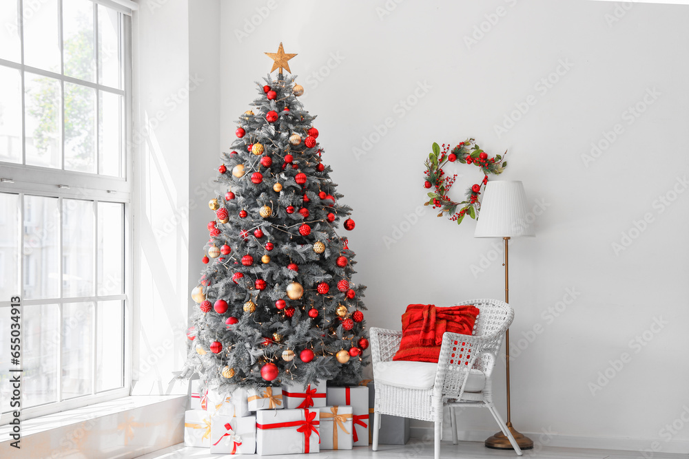 Gift boxes under Christmas tree and white armchair in festive room