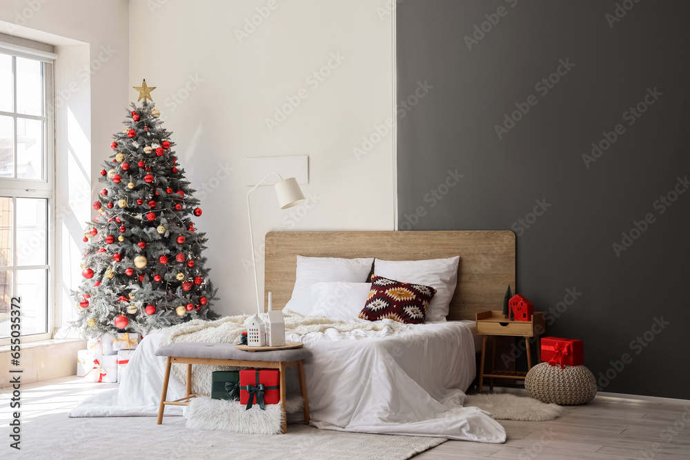 Interior of festive bedroom with comfortable bed and Christmas tree