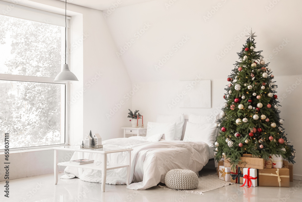 Interior of festive bedroom with comfortable bed and Christmas tree