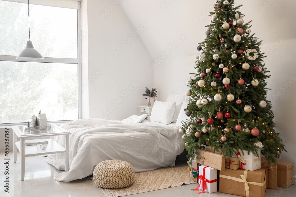 Interior of festive bedroom with comfortable bed and Christmas tree