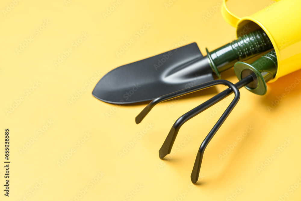 Watering can with gardening rake and shovel on yellow background