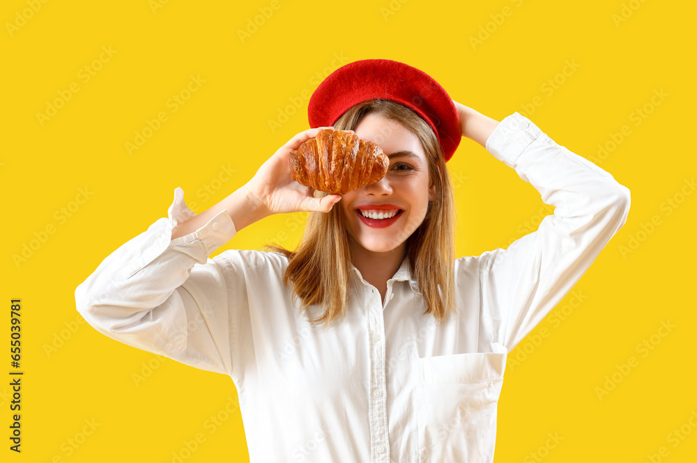 Beautiful stylish young woman in beret with tasty croissant on yellow background