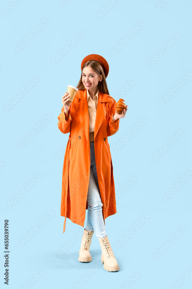 Beautiful young woman with tasty croissant and cup of coffee on blue background