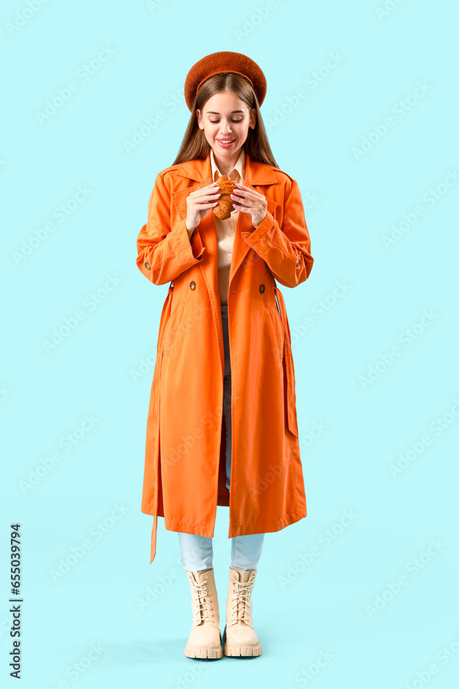 Beautiful happy young woman in beret with tasty croissant on blue background