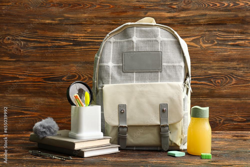 Grey school backpack with bottle of juice, books and stationery on wooden background