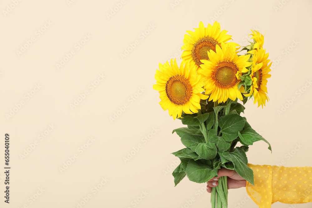 Young woman with beautiful sunflowers on beige background