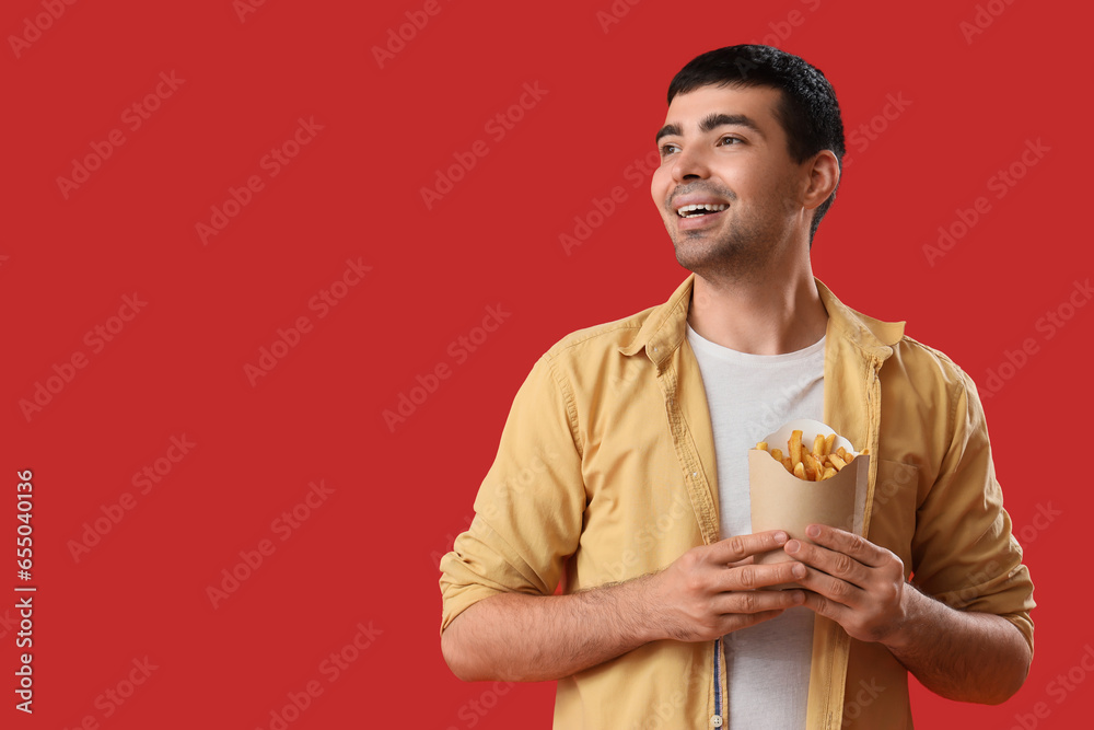 Young man with french fries on red background