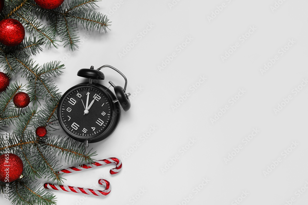 Alarm clock with Christmas tree branches and candy canes on white background