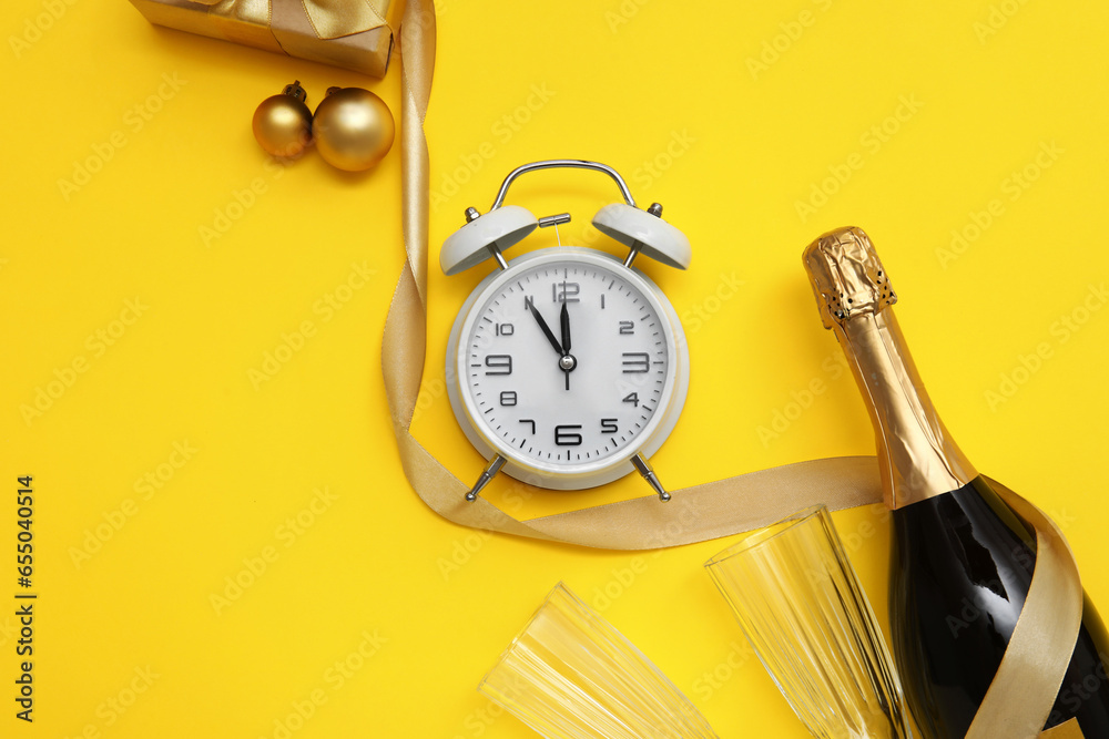 Alarm clock with Christmas champagne and ribbon on yellow background