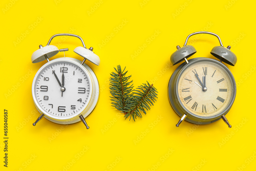 Alarm clocks with Christmas tree branches on yellow background