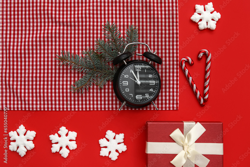 Alarm clock with Christmas tree branches, snowflakes and gift boxes on red background