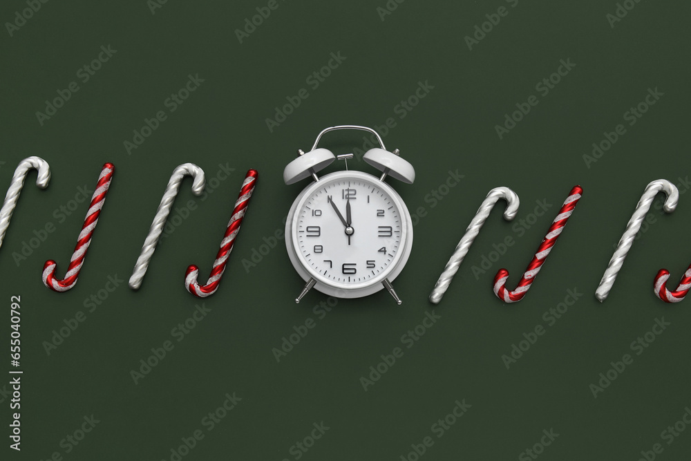 Alarm clock and candy canes on green background