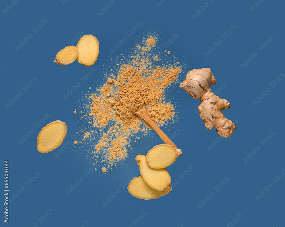 Flying slices of fresh ginger root and wooden spoon with dried powder on blue background