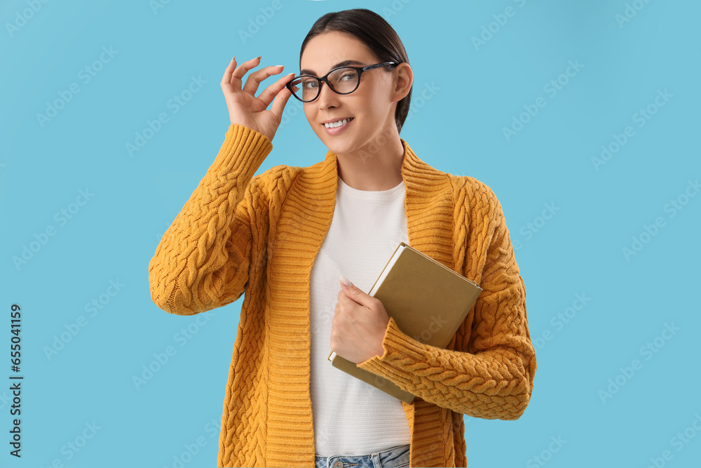 Young female teacher with book on light blue background