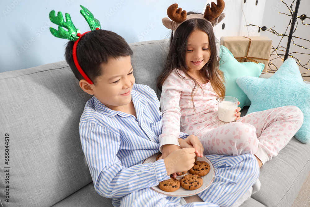 Cute little children in pajamas, with cookies and glass of milk on Christmas eve at home