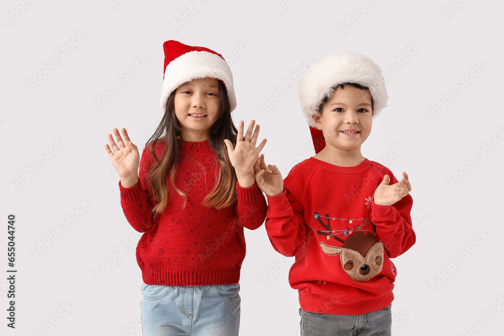 Cute little children in winter sweaters and Santa Claus hats on light background