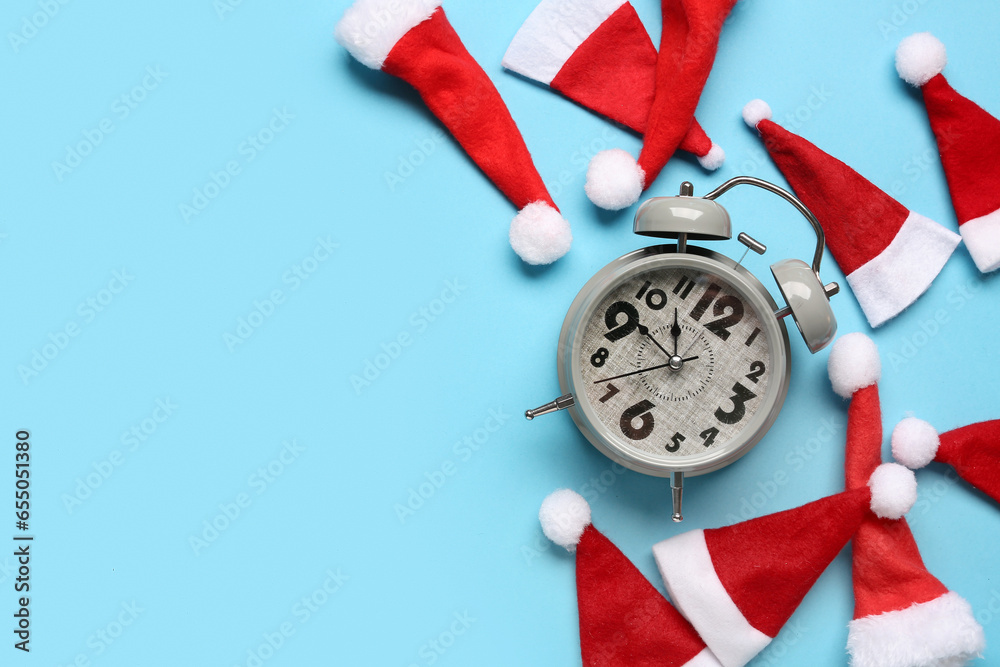 Composition with alarm clock and Santa hats on color background