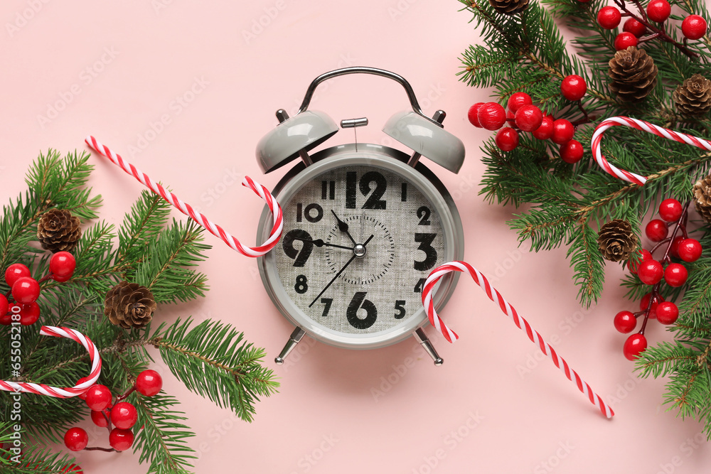 Alarm clock and Christmas tree branches with candy canes on pink background