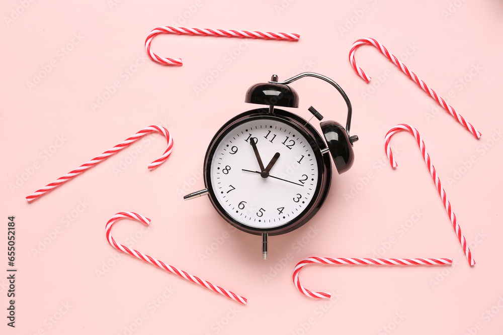 Alarm clock with Christmas candy canes on pink background