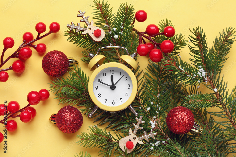 Alarm clock and Christmas tree branches with balls on yellow background