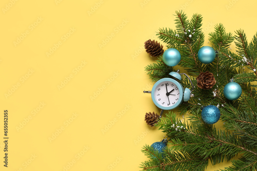 Alarm clock and Christmas tree branches with balls on yellow background