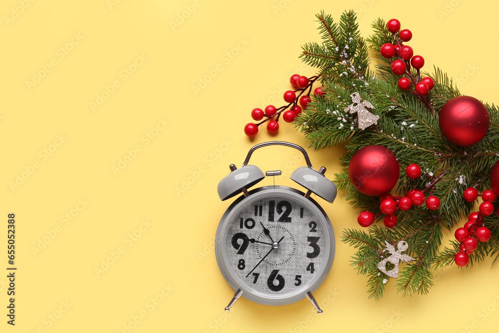 Alarm clock and Christmas tree branches with balls on yellow background