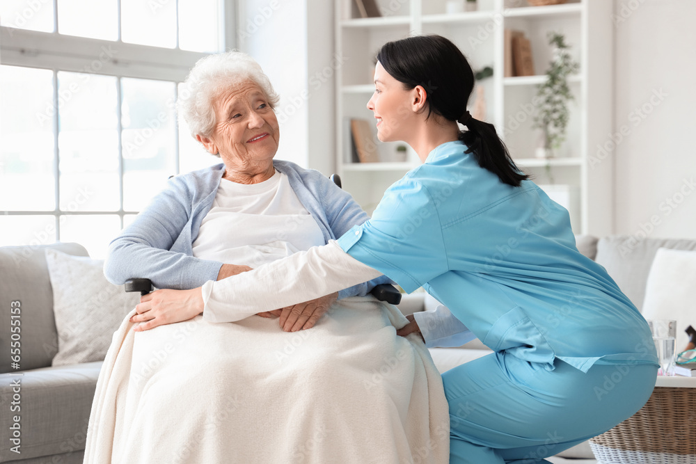 Female nurse caring about senior woman in wheelchair at home