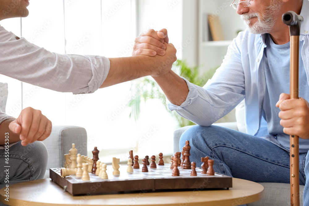 Senior man with his son playing chess at home, closeup