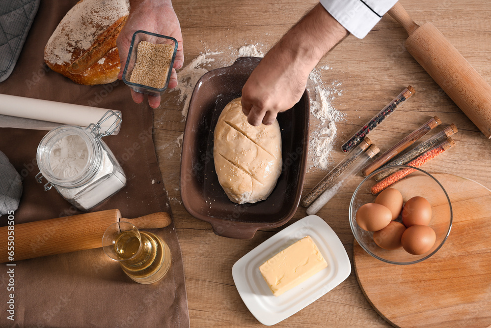 Young chef sprinkling raw bread with sesame seeds in bakery