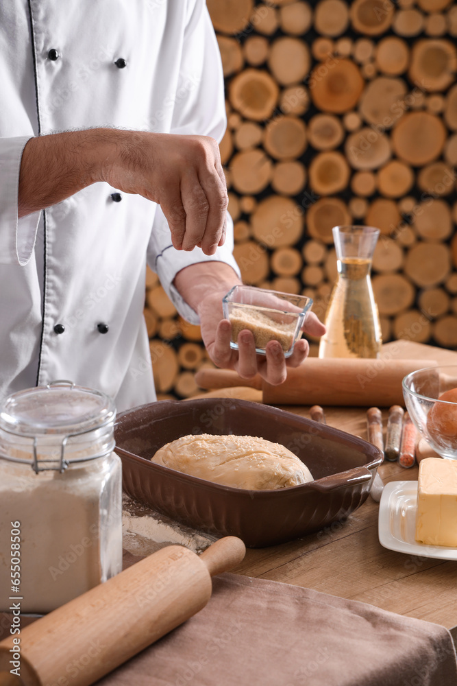 Young chef sprinkling raw bread with sesame seeds in bakery