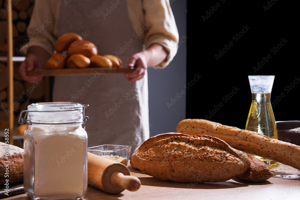 Young chef holding board with fresh buns in bakery, closeup