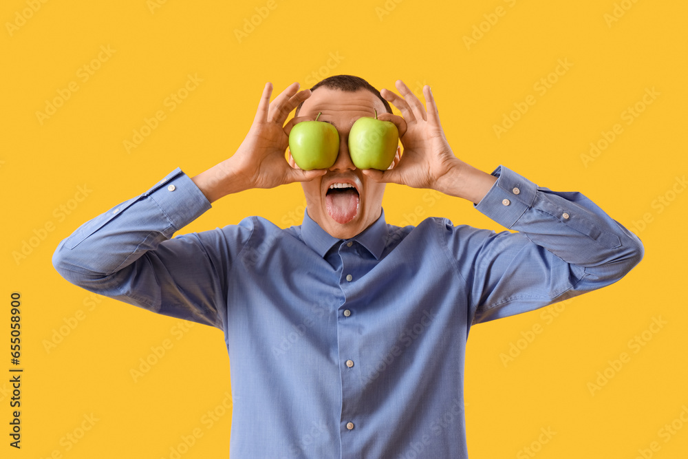 Young man with tasty apples showing tongue on yellow background