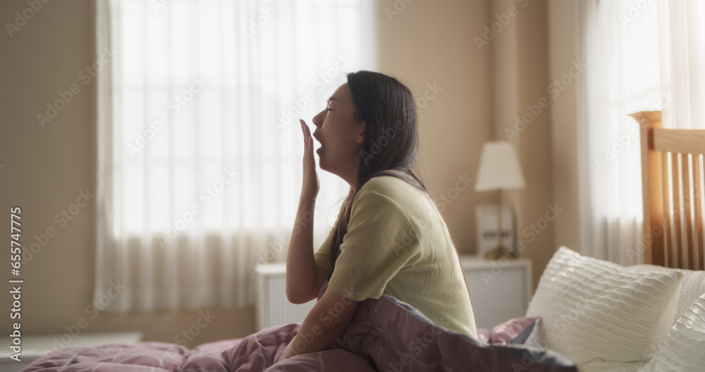 Young Attractive Korean Woman Waking up in the Morning, Stretching Her Neck and Looking Around the Room, Sun Shines From the Windows into Bedroom. Asian Girl Starting Leisure Weekend Slowly at Home