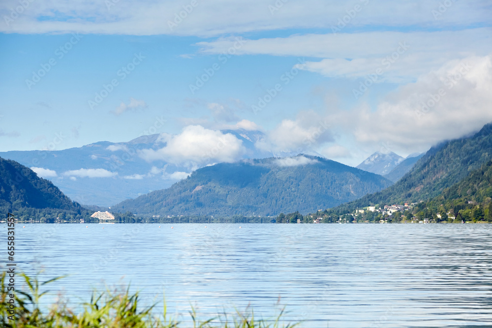 Lake Ossiacher See, Ossiach, Carinthia, Austria. Beautiful summer mountain landscape. Alpine lake surrounded by mountains, slopes of which are covered with forest and white clouds