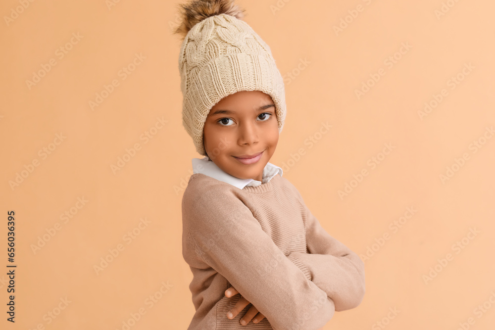 Cute African-American boy in warm winter clothes on beige background