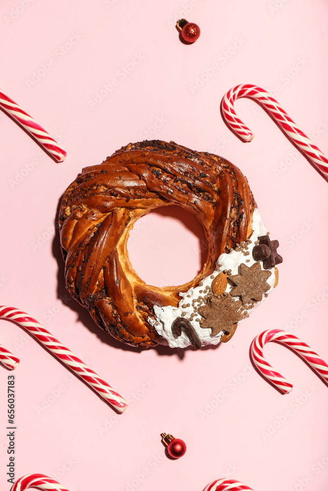 Composition with tasty Christmas pastry wreath, candy canes and balls on pink background