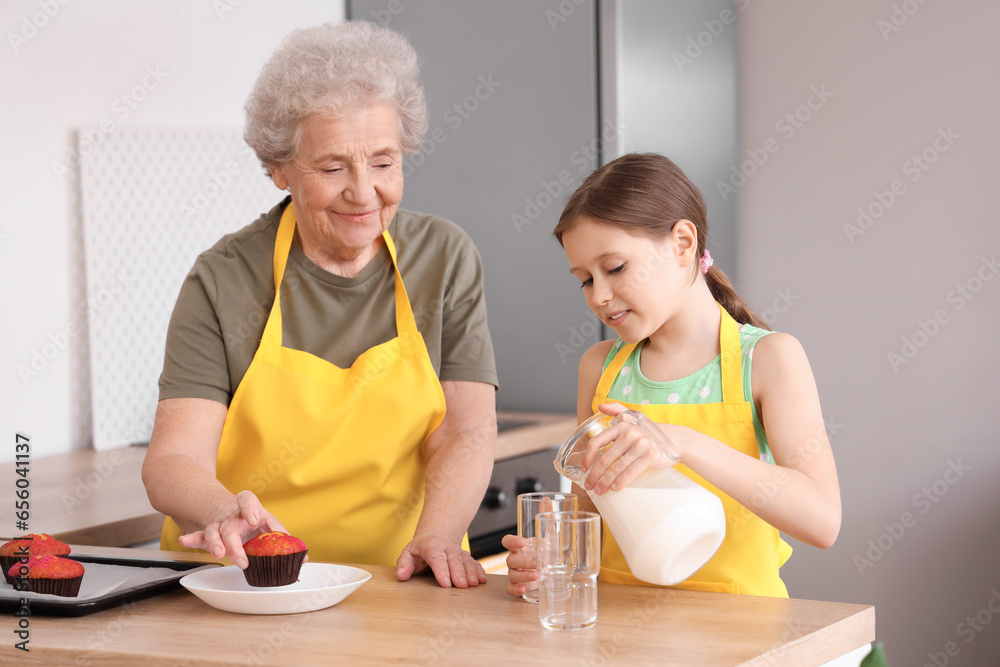 Senior woman and her little granddaughter pouring milk into glass in kitchen