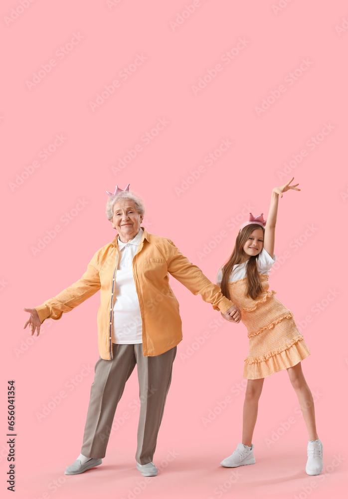 Little girl with her grandmother in crowns dancing on pink background