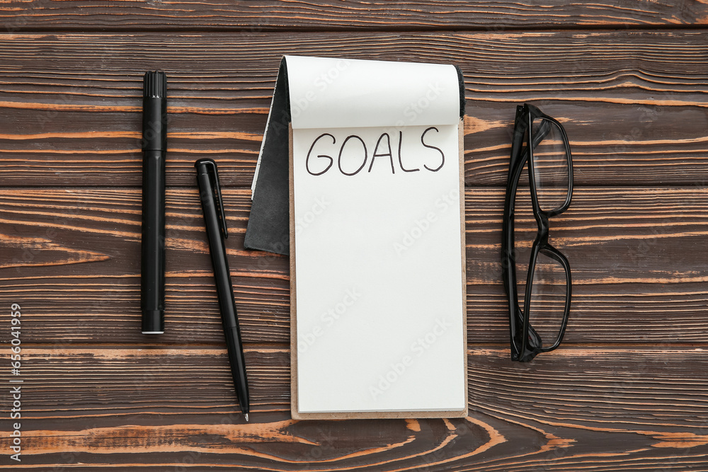 Notebook with empty to do list, stationery and eyeglasses on brown wooden background. New year goals