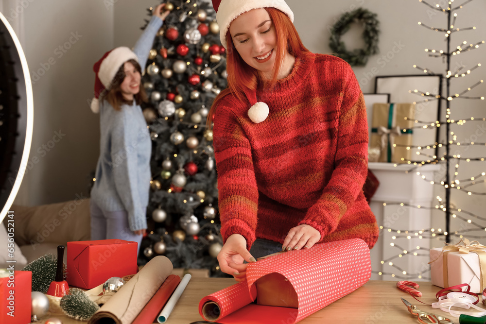 Young woman wrapping Christmas gift while recording video at home