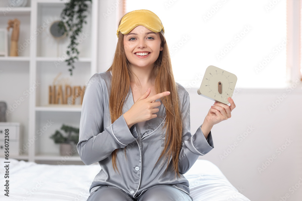 Beautiful young woman in pajamas pointing at clock in bed at home